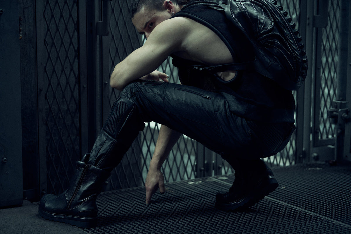 Seated model wearing a black SYZMIC backpack and black mesh tank top.