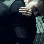 SYZMIC black panelled long-sleeve top with the model leaning forward, showing mesh and sleeve details.