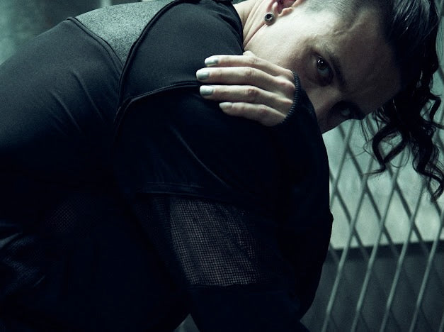SYZMIC black panelled long-sleeve top with the model leaning forward, showing mesh and sleeve details.