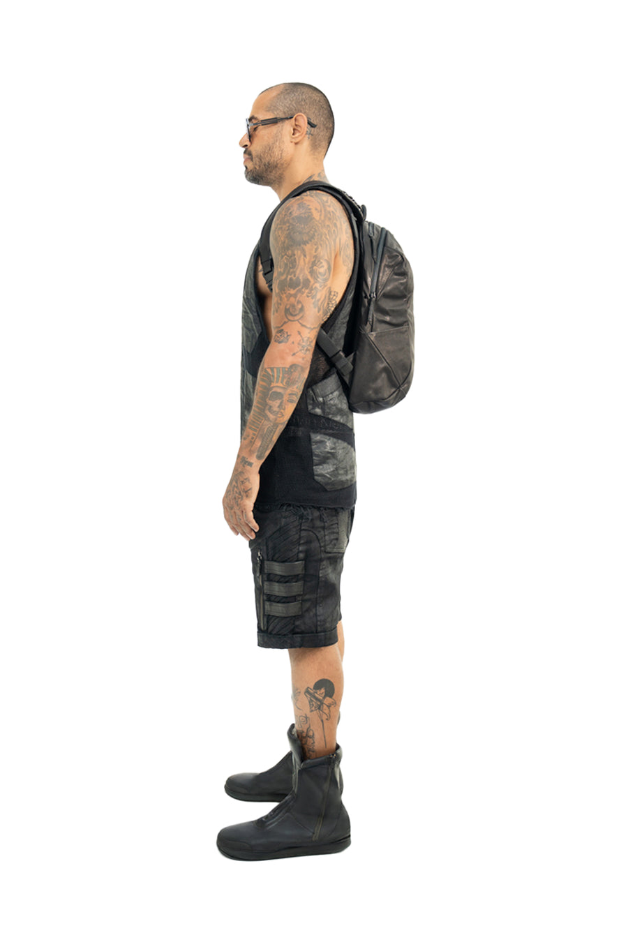 Side profile of a tattooed model wearing the Syzmic Studio black leather backpack. The backpack’s sleek, contoured shape sits comfortably on the back, blending avant-garde fashion with practical design