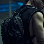 Black sculptural SYZMIC backpack worn over a sleeveless mesh top, rear three-quarter view.