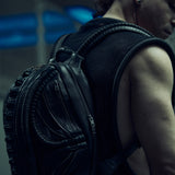 Black sculptural SYZMIC backpack worn over a sleeveless mesh top, rear three-quarter view.