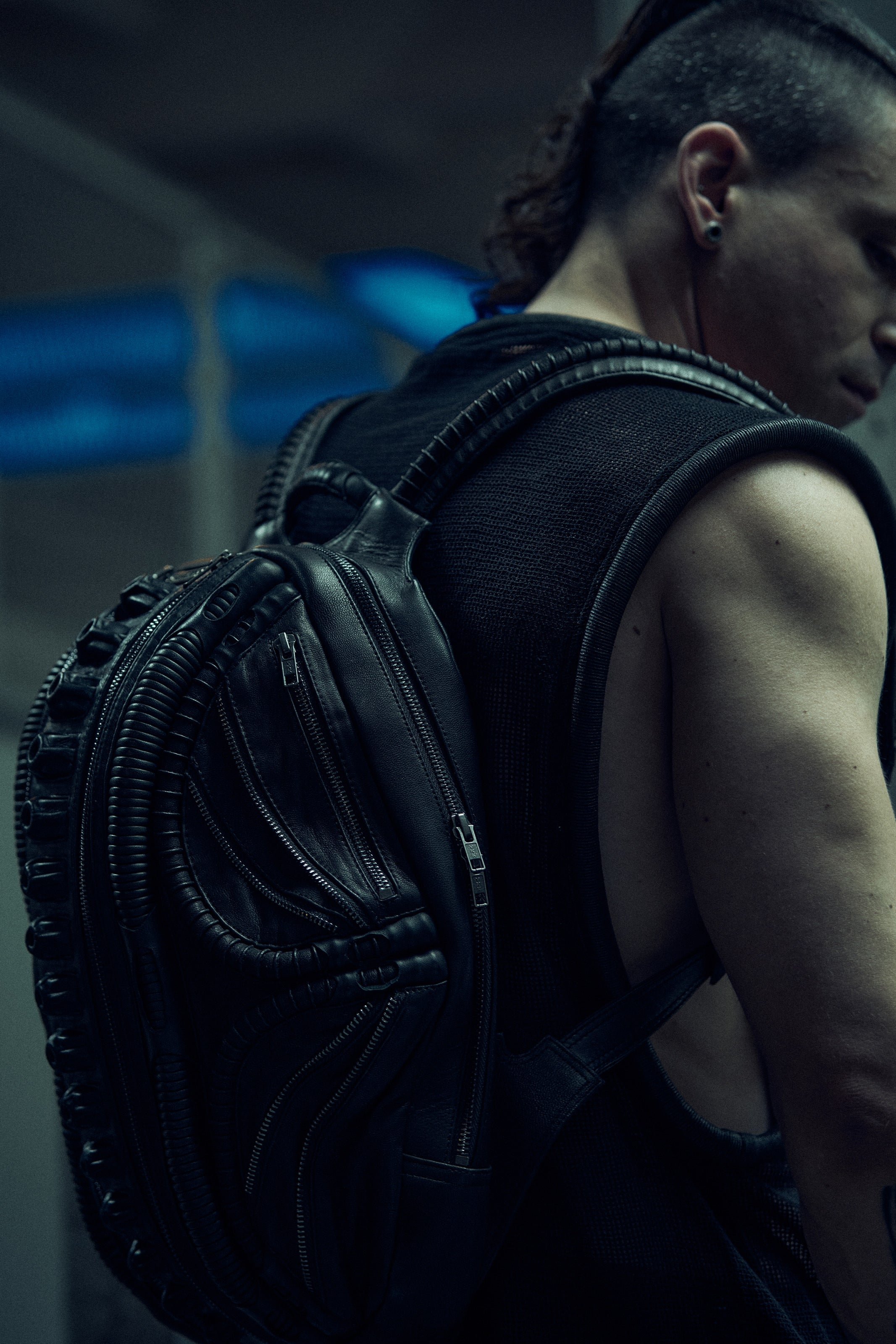 Black sculptural SYZMIC backpack worn over a sleeveless mesh top, rear three-quarter view.