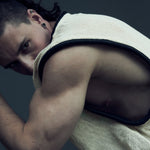 White SYZMIC EIDOS-212 tank top worn in a seated side pose, with black tubular trim.