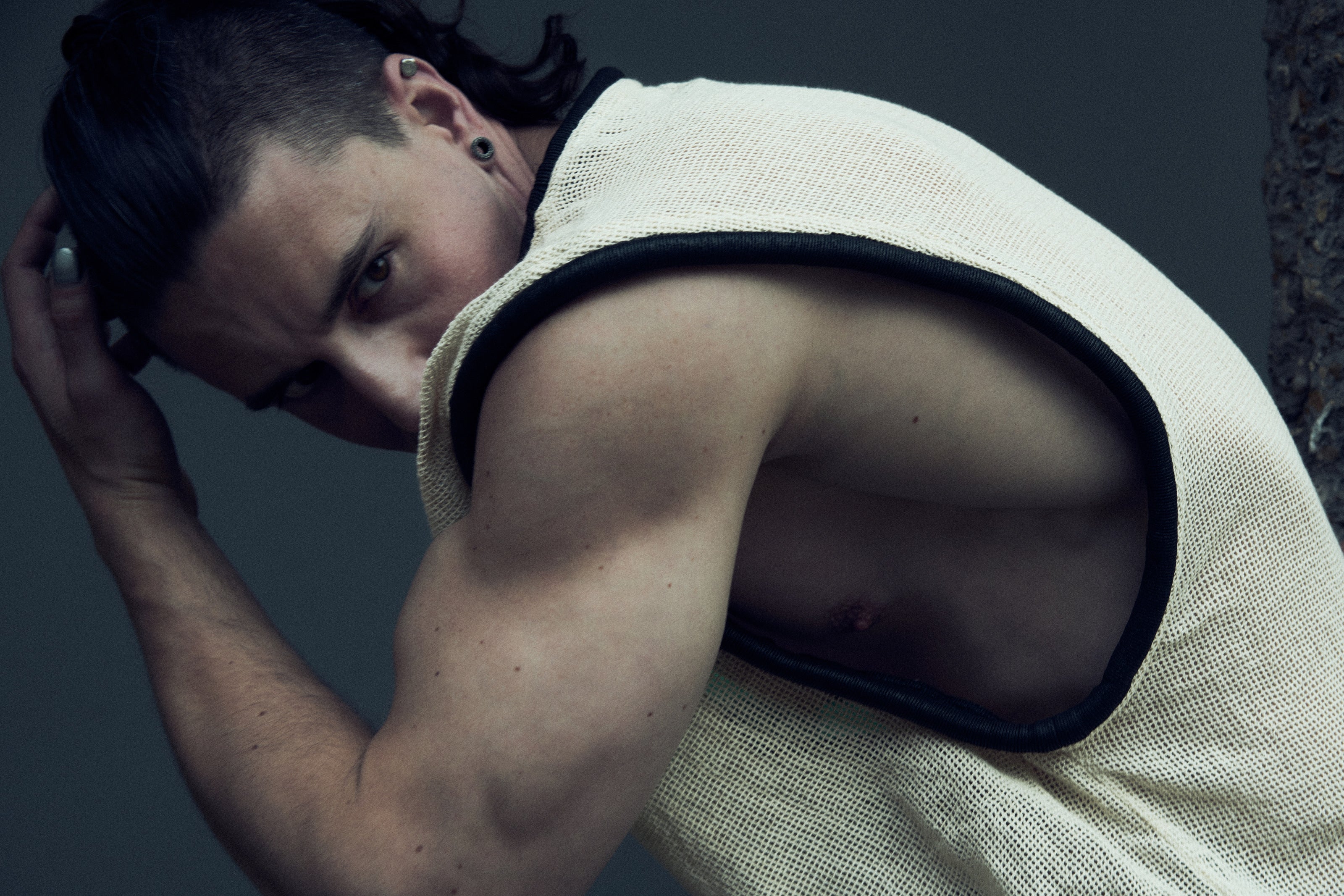 White SYZMIC EIDOS-212 tank top worn in a seated side pose, with black tubular trim.