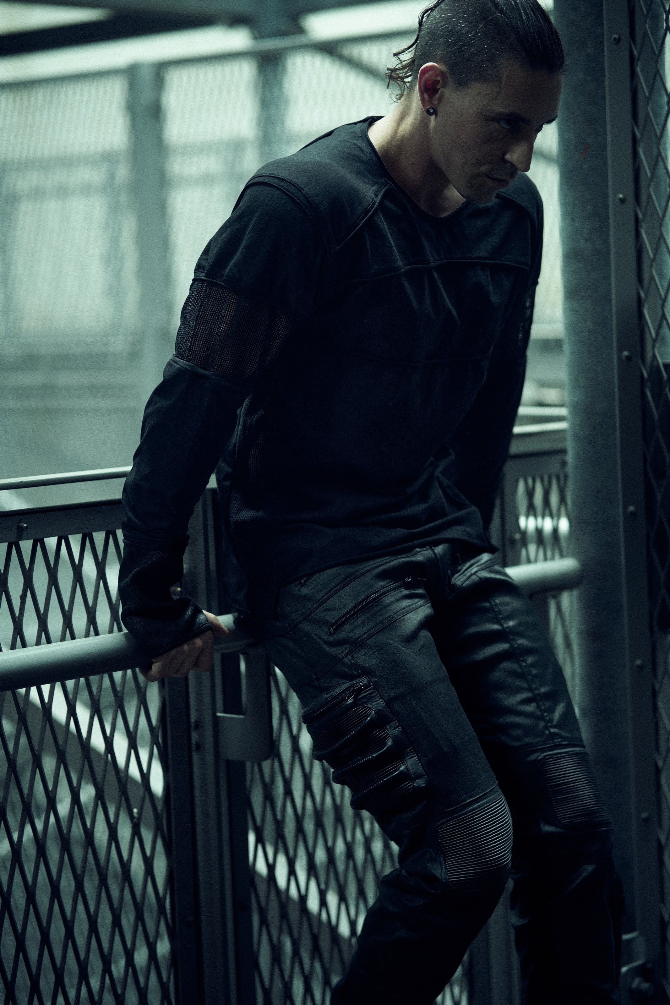 Black SYZMIC EIDOS-215 long-sleeve top worn beside a metal railing, front three-quarter view.