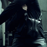 Black SYZMIC EIDOS-215 long-sleeve top, side view with a sculptural bag.