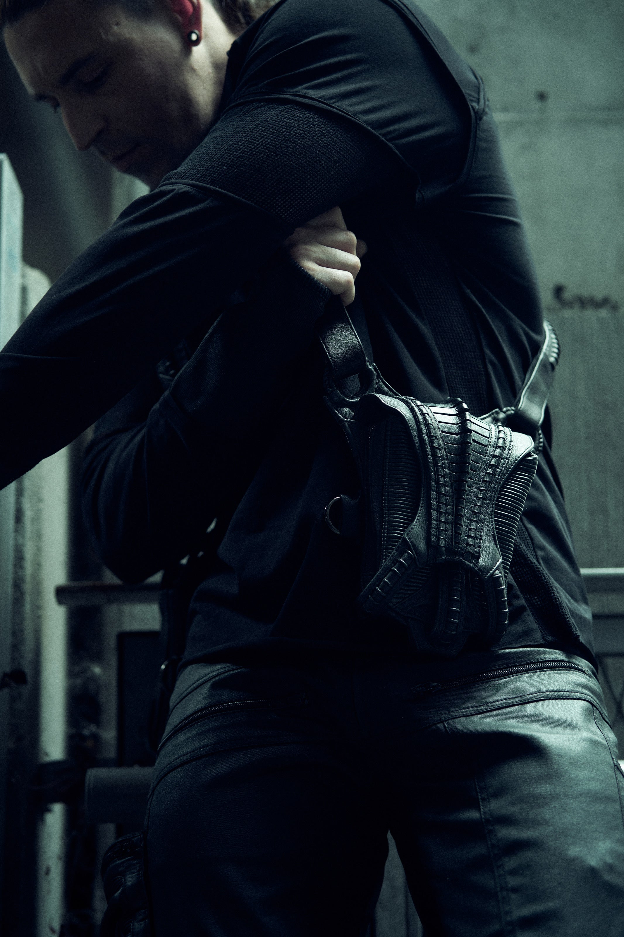 Black SYZMIC EIDOS-215 long-sleeve top, side view with a sculptural bag.