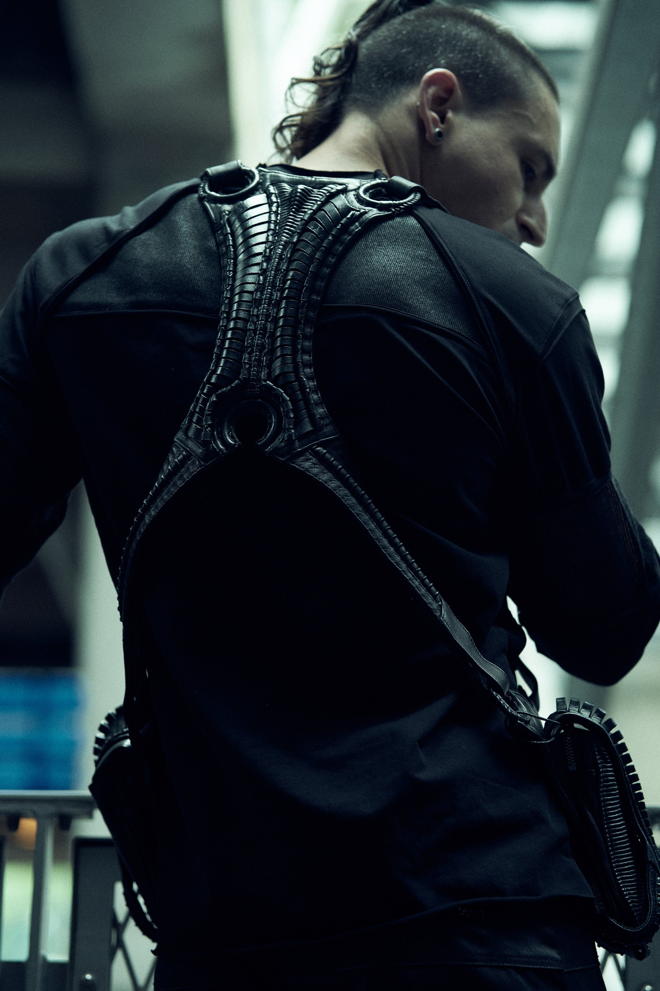 Rear view of the black SYZMIC EIDOS-215 long-sleeve top worn beneath a backpack.