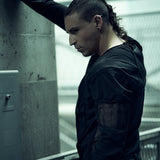 Black SYZMIC EIDOS-215 long-sleeve top, side portrait with one arm raised.