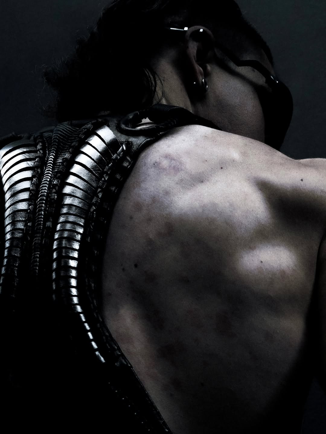 Rear close-up of Flo wearing the black SYZMIC HYLO-501 leather holster bag, showing its sculpted vertebral back panel. Photography by Lazar.
