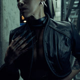 Lily Gatins wearing the black SYZMIC JACKET EIDOS-408, close-up showing the sculpted shoulder panels and coiled trim. Photography by Nox / Lux.