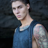 Leather piping veins emerge and submerge into straps of a holster bag worn on top of waxed textured men's tank top