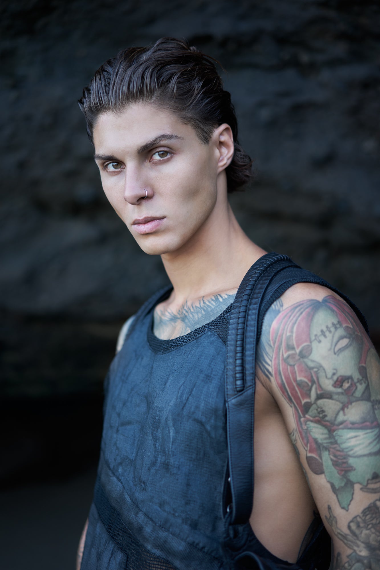 Leather piping veins emerge and submerge into straps of a holster bag worn on top of waxed textured men's tank top