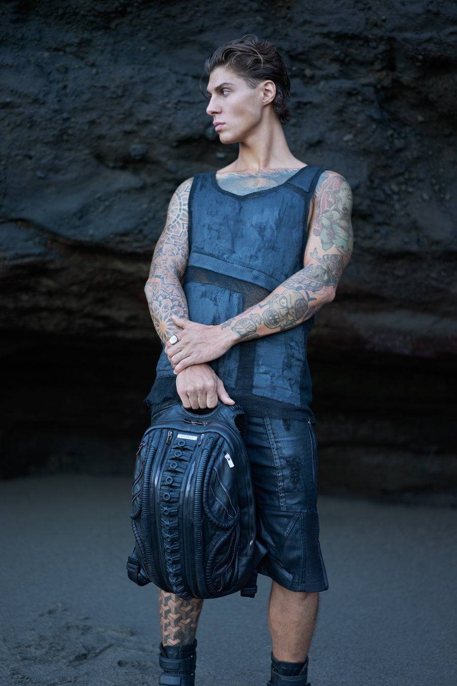Men's avant-garde streetwear with dark post-apocalyptic clothing and leather backpack, alternative tank top and utility cargo shorts